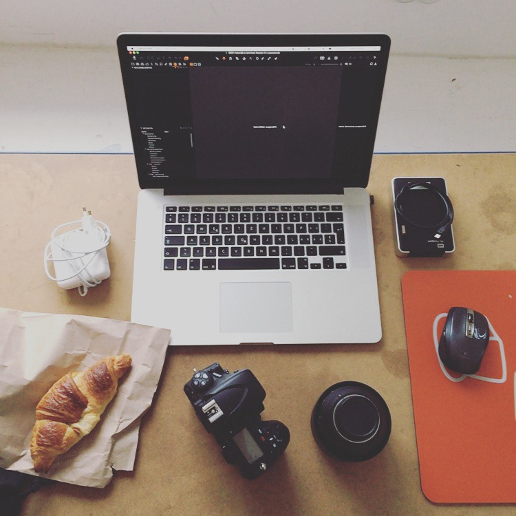 Laptop, Kamera und Croissant auf dem Schreibtisch